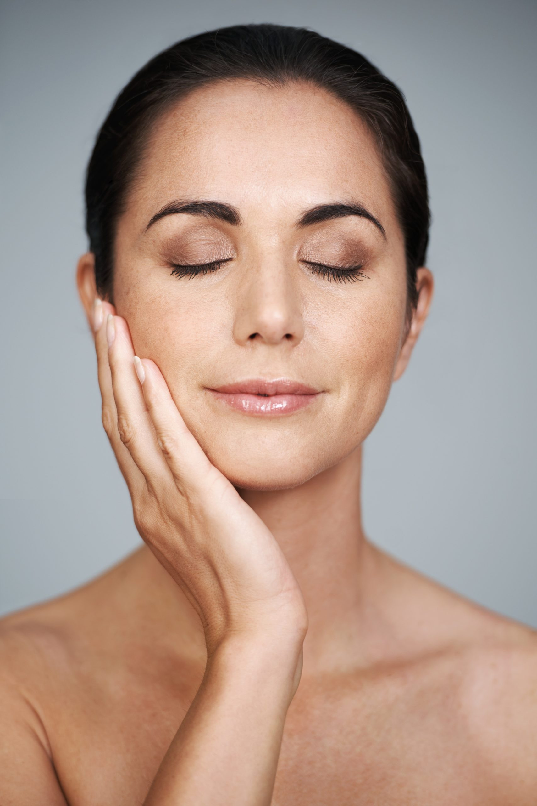Beauty, mature and skincare of woman touching face with makeup at studio isolated on gray background. Cosmetics, glow and hand of model in facial treatment for dermatology, anti aging and eyes closed.