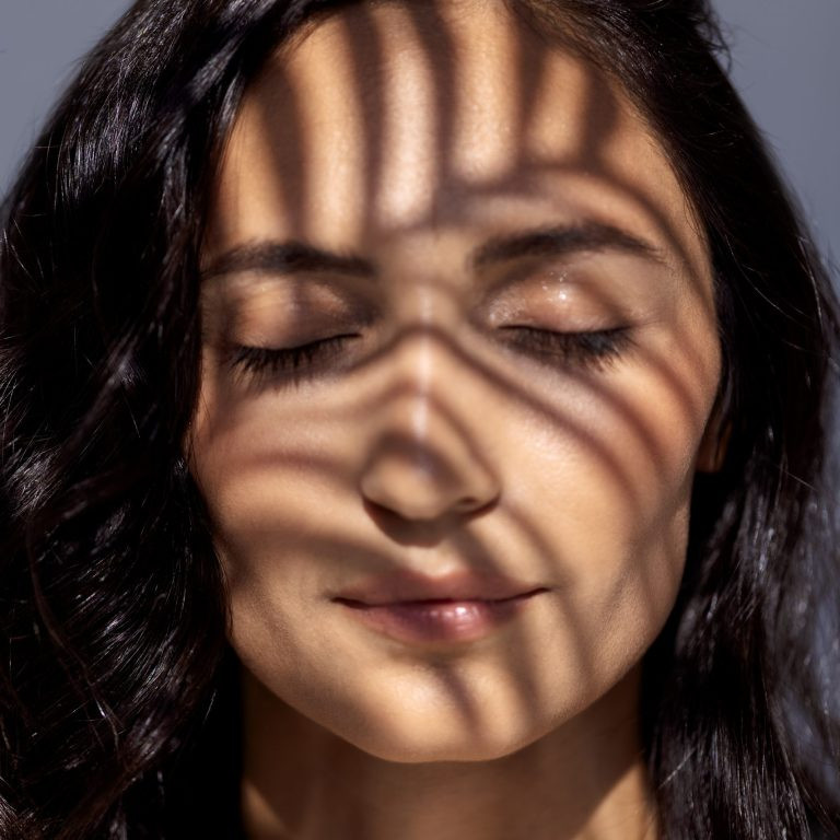 A close-up beauty portrait of a young attractive woman with closed eyes and a green leaf. A beautiful brunette with healthy clear skin and a fern leaf. Cosmetic, wellness, skincare, spa concept.